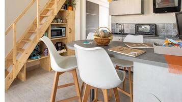 Een moderne keuken met een ingebouwde magnetron, een groot keukenblok met zitplaatsen, en een houten trap die naar een vide leidt.