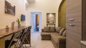 A modern living room with a sofa, a dining table with chairs, a TV, and a kitchen area with a refrigerator. - Rome Centro-Repubblica Apartment  (Roma)