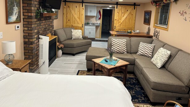 A cozy living room with a fireplace, a sofa, a dining table, and a kitchen area visible through an open door. - Jaggi Swiss Gasthaus  (Monticello)