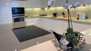 Een moderne keuken met witte kastjes, een zwarte inductiekookplaat en een wijnfles op een decoratieve standaard.