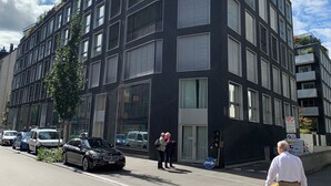 Een modern gebouw met een donkere gevel, grote ramen en een hoingang.