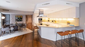 Een moderne keuken met een centraal eiland, barkrukken en een eetgedeelte met een tafel en stoelen.