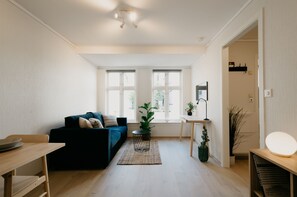 A modern living room with a dark blue sofa, a small round table, a potted plant, and a bright floor lamp. - Bergen Beds - Studio Ground level (Bergen)