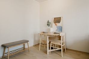 A corner room with a wooden bench, a small table with a vase and a bowl, and a painting on the wall.