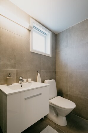 A modern bathroom with a white sink, a toilet, and a window above the sink. - Bergen Beds - Studio Ground level (Bergen)