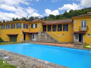 Stunning two-story building with a stone staircase, multiple windows, and a balcony overlooking a serene pool surrounded by a lush lawn and walkway.
