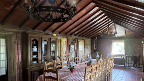 A rustic dining area with a long wooden table set for six, flanked by wooden chairs. A chandelier hangs from the ceiling, and a stone wall with a window is visible in the background. - House with pool and barbecue (Valença)