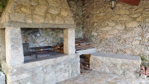 A stone-built outdoor fireplace with a metal grate and logs stored inside. - House with pool and barbecue (Valença)