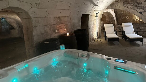 Une pièce aux murs de pierre, équipée d’un jacuzzi, de deux fauteuils et d’un lampadaire sur trépied.