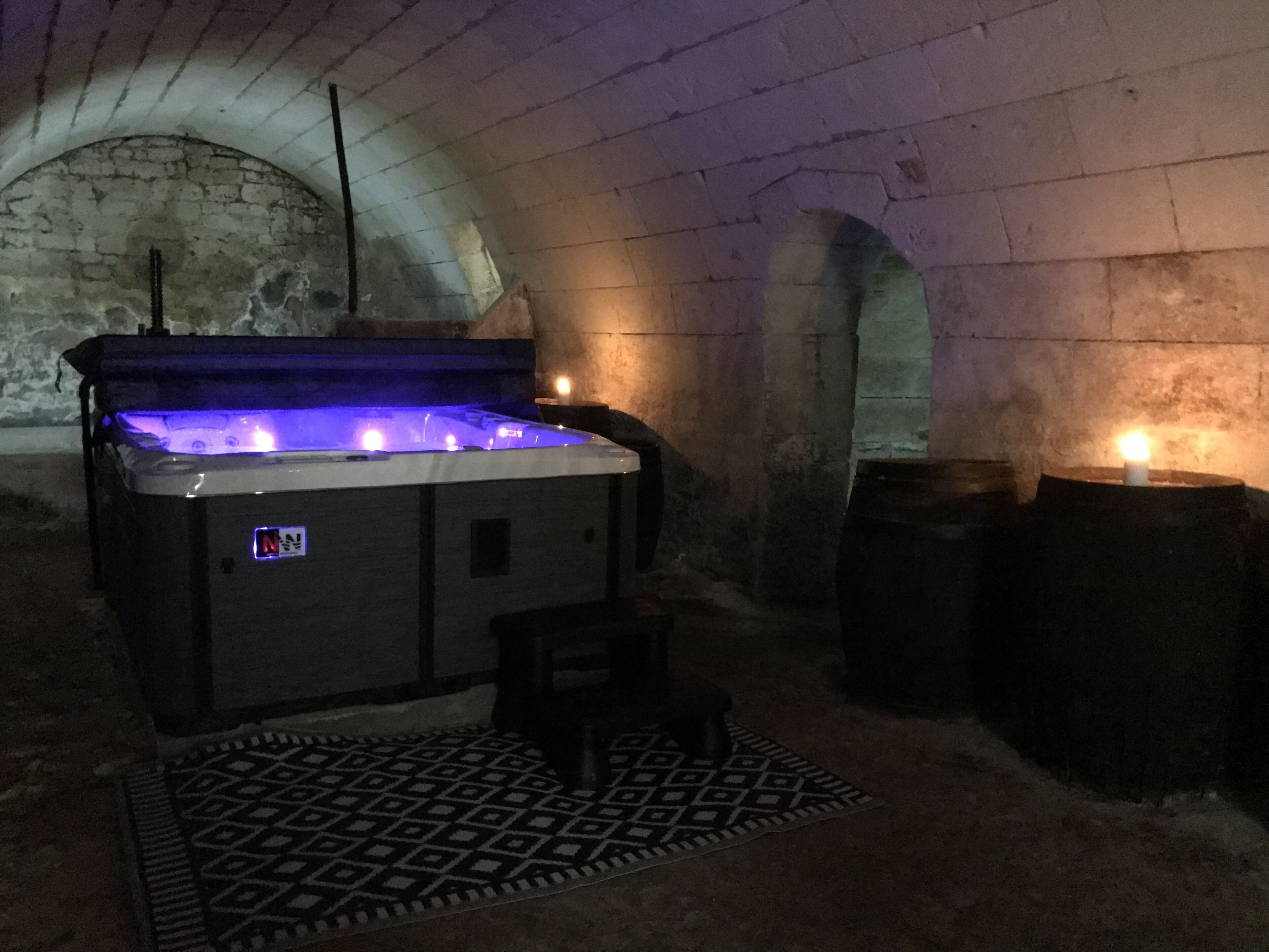 A hot tub in a stone-walled room with a patterned rug and candles.