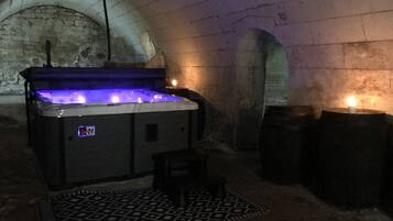 A hot tub in a stone-walled room with a patterned rug and candles.