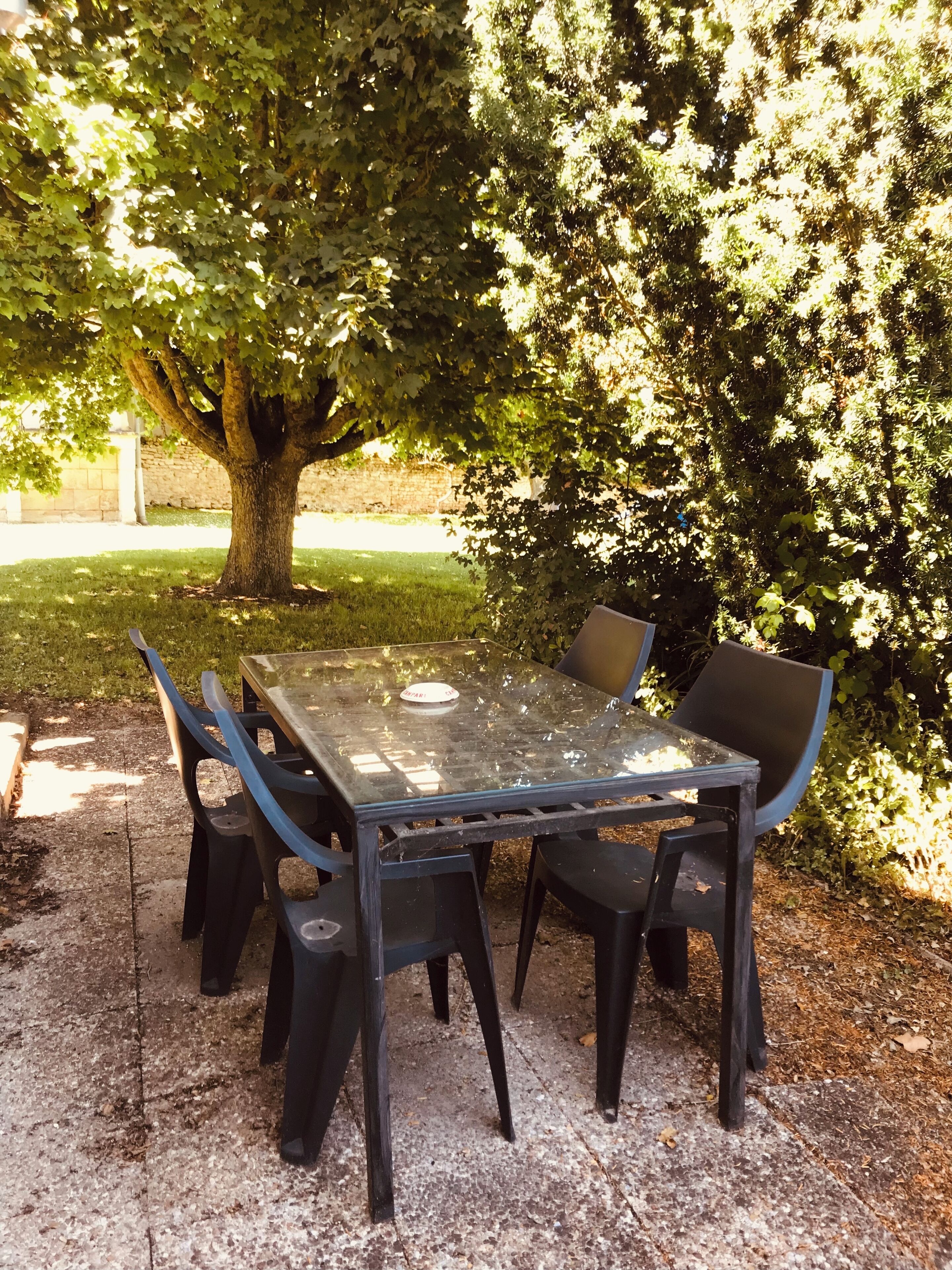 An outdoor table and chairs set on a concrete surface, surrounded by trees and a grassy area.