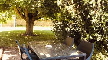 An outdoor table and chairs set on a concrete surface, surrounded by trees and a grassy area.
