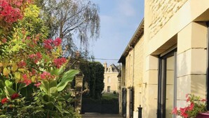 Un chemin pavé mène à un bâtiment à l’architecture traditionnelle, entouré d’une végétation luxuriante et de plantes en fleurs.