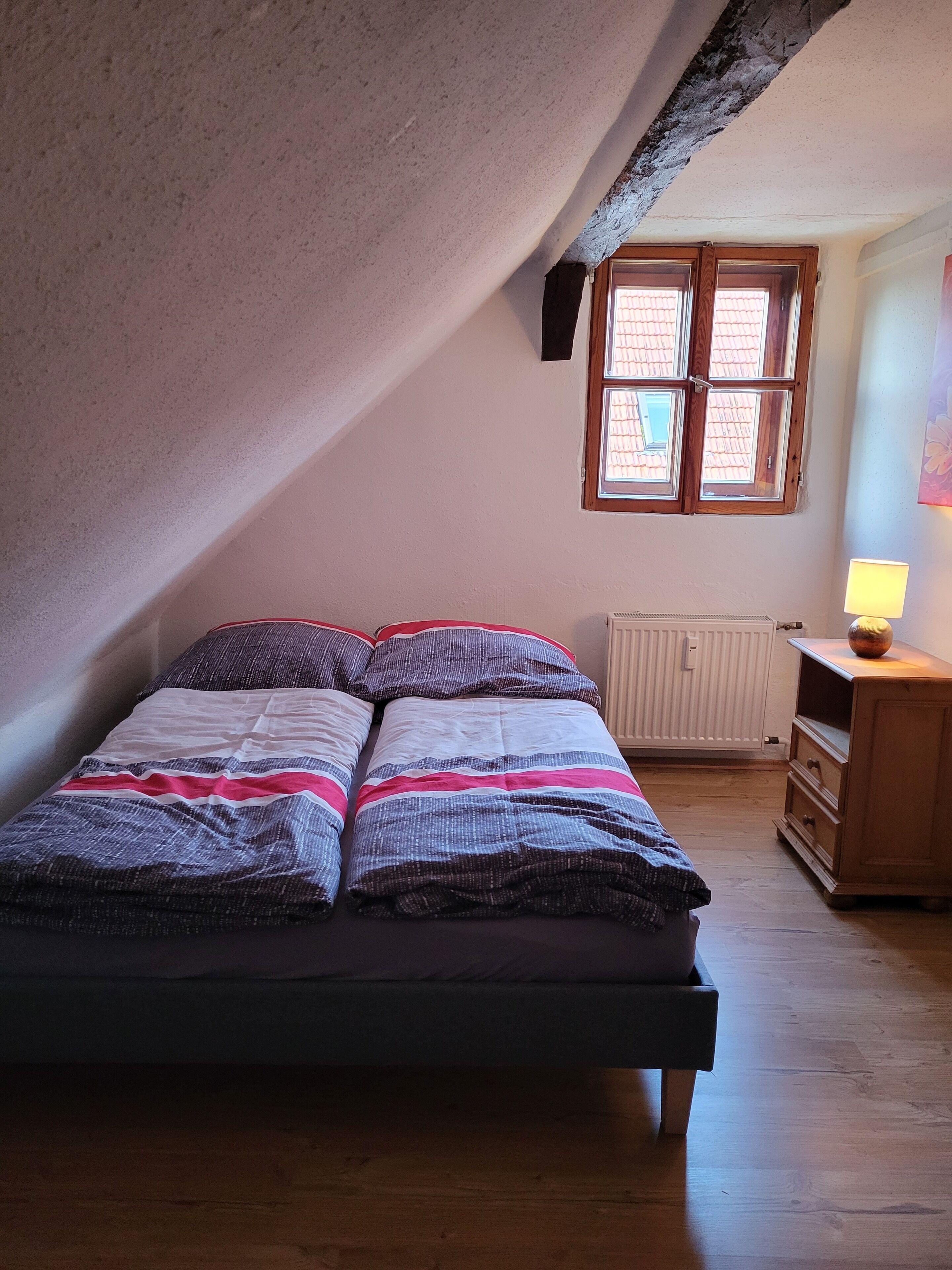Quarto com cama, janela, radiador e abajur.