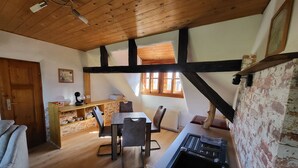 A cozy room with a wooden ceiling, a dining area with a table and chairs, a kitchen with a sink, and a window with wooden shutters. - Cozy vacation apartment for 1 to 4 people. Perfect for a little time out  (Frielendorf)