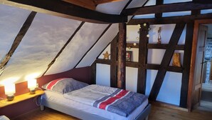 A cozy attic bedroom with a sloped ceiling, exposed wooden beams, a bed with a striped blanket, bedside lamps, and a star decoration. - Cozy vacation apartment for 1 to 4 people. Perfect for a little time out  (Frielendorf)