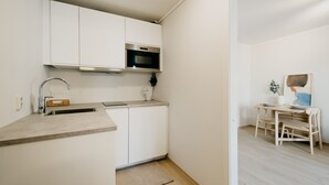 A compact kitchen with white cabinets, a stainless steel microwave, and a wooden dining table with chairs.