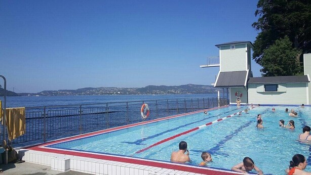 A swimming pool with a view of the sea, surrounded by a fence and a lifeguard stand.