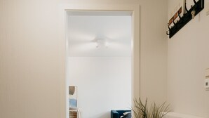 A hallway with a wooden floor, a white wall, a black shelf with decorative items, and a potted plant.