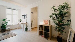 A bright, modern living room with a large window, a wooden floor, and several potted plants.