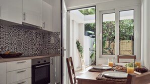 A modern kitchen with white cabinets, patterned backsplash, and a dining area with wooden table and chairs. - One Bedroom Apartment (Zakynthos)