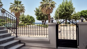 A gated entrance with a view of the sea, palm trees, and a staircase leading to a building. - One Bedroom Apartment (Zakynthos)