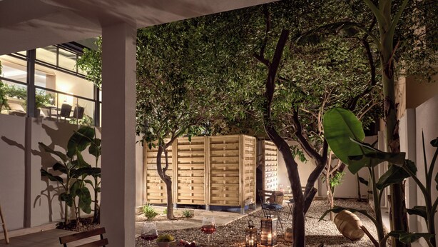 A patio area with a wooden table, chairs, and a bench. There are potted plants and a wooden fence in the background. - One Bedroom Apartment (Zakynthos)