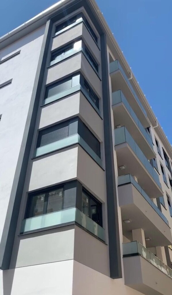 A modern multi-story building with a flat facade, large windows, and balconies.