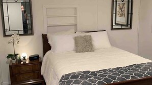 A bedroom with a wooden bed, white bedding, a nightstand with a lamp, and two arched windows. - Cozy 1BR Cottage Near Lake, Trails & City Access (Kenmore)