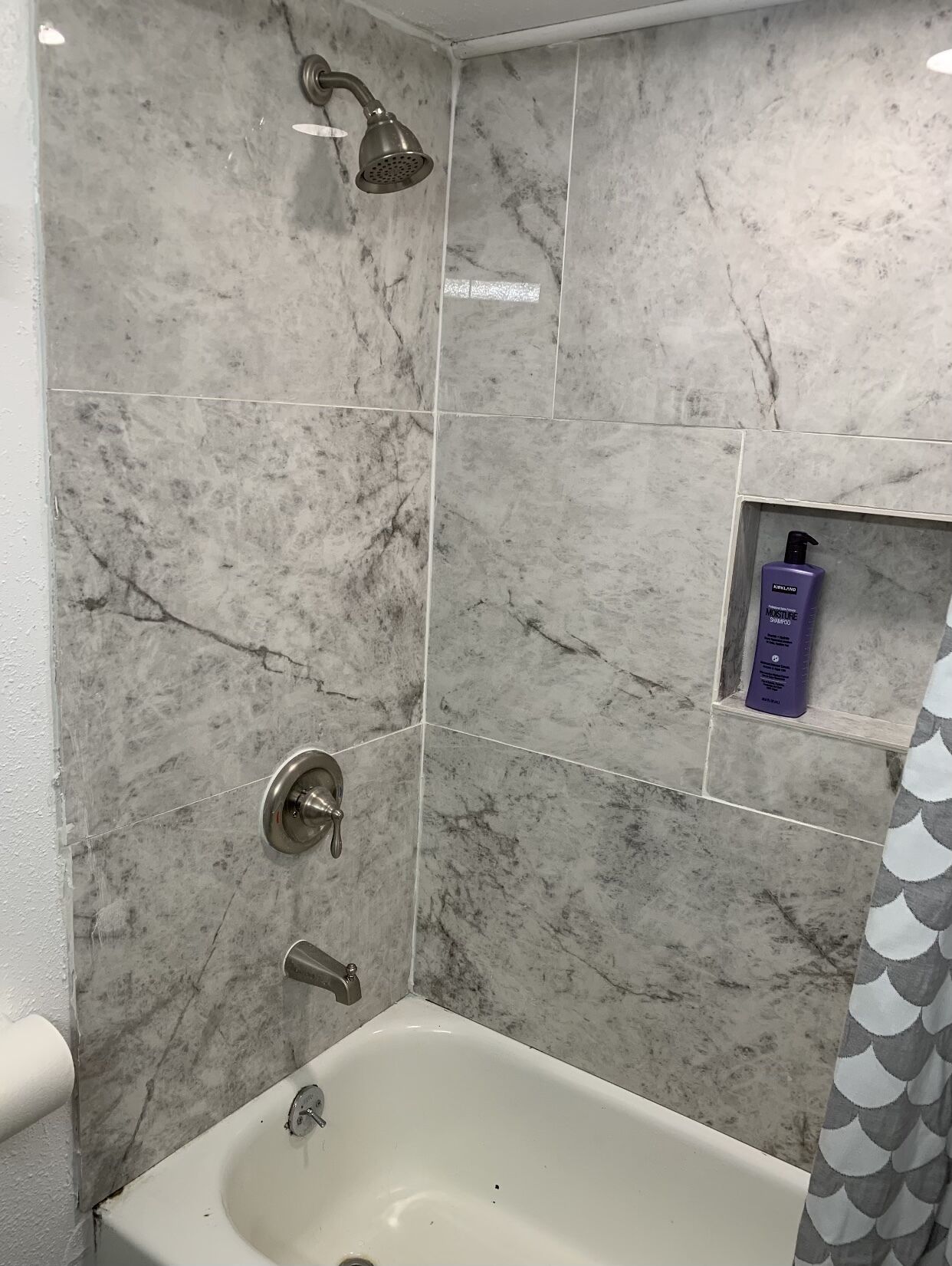Un bagno con una vasca, una doccetta e uno scaffale con articoli da toilette.