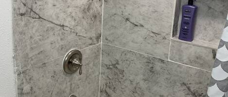 Un bagno con una vasca, una doccetta e uno scaffale con articoli da toilette.
