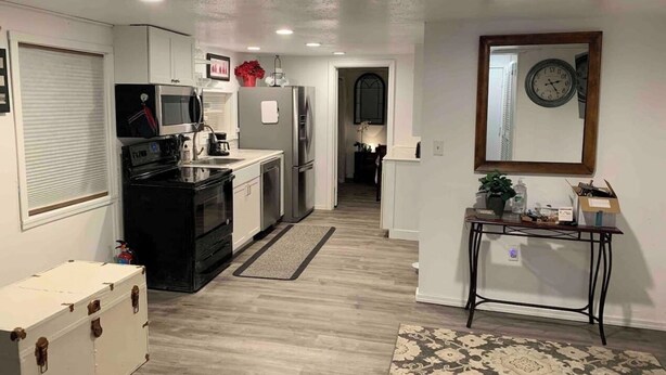 A compact kitchen with a microwave, stove, and refrigerator. There's a small table with a clock and a mirror on the wall. - Cozy 1BR Cottage Near Lake, Trails & City Access (Kenmore)