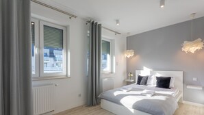 Ein modernes Schlafzimmer mit einem großen Bett, grauen Vorhängen und Blick auf Gebäude.