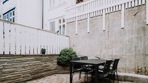 Eine Terrasse mit einer Steinsäule, einem weißen Zaun und einem Tisch mit Stühlen.