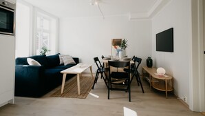 Ein modernes Wohnzimmer mit einem dunkelblauen Sofa, einem Holzespeisetisch mit Stühlen, einem kleinen Couchtisch und einem großen Fenster, das für natürliches Licht sorgt.