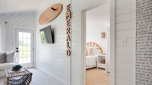 Una habitación con paredes de madera blanca, una cama con cabecera de madera, una pequeña mesa con una planta y una pared con mensajes motivacionales.