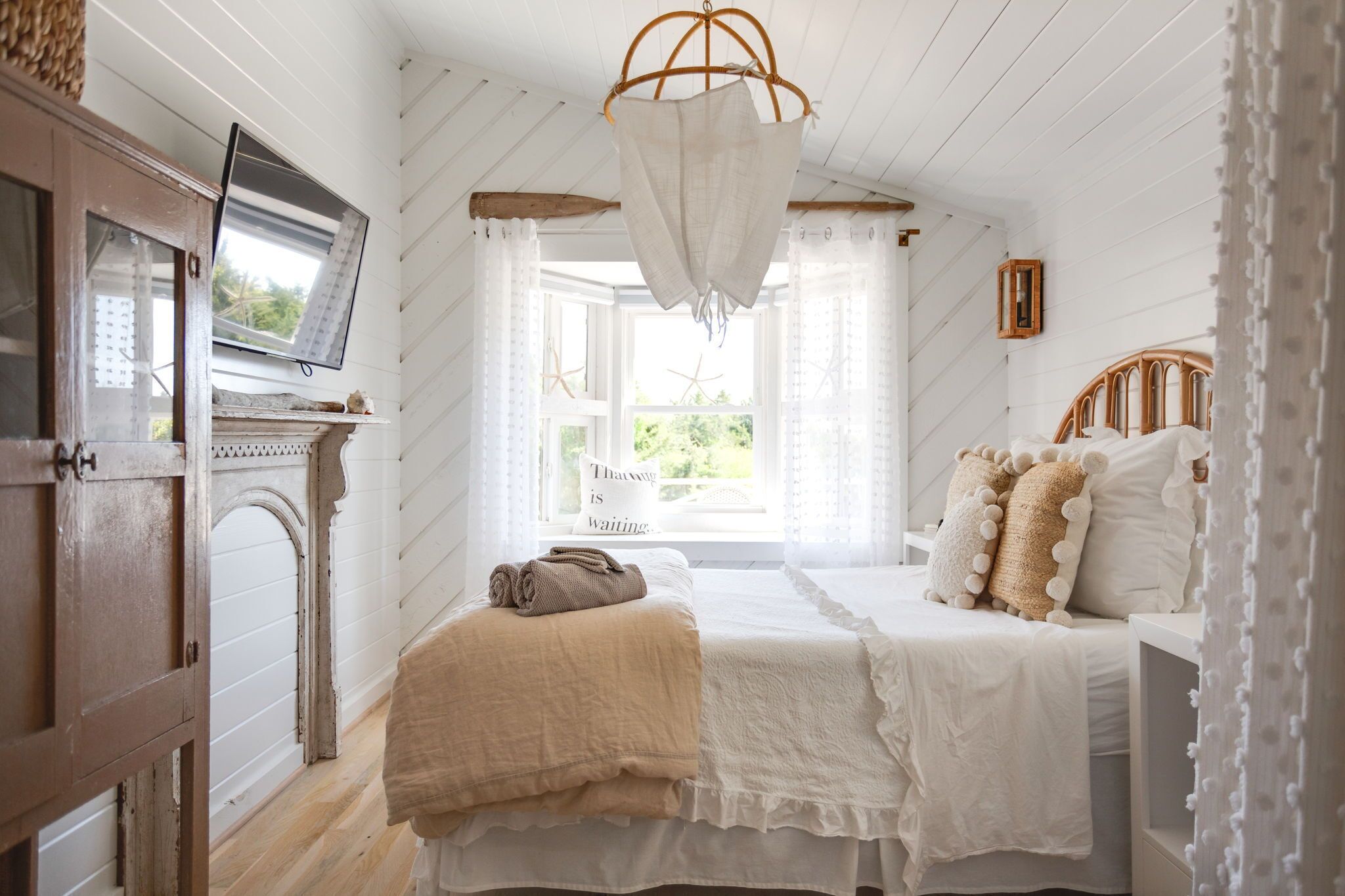 A bedroom with a bed, a wooden wardrobe, a television, and a window with curtains.
