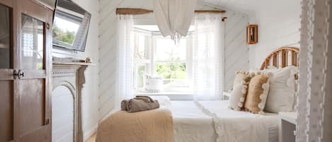 A bedroom with a bed, a wooden wardrobe, a television, and a window with curtains.