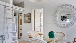 Una habitación con una escalera blanca, sillas de mimbre, una mesa de vidrio y un espejo con marco decorativo.