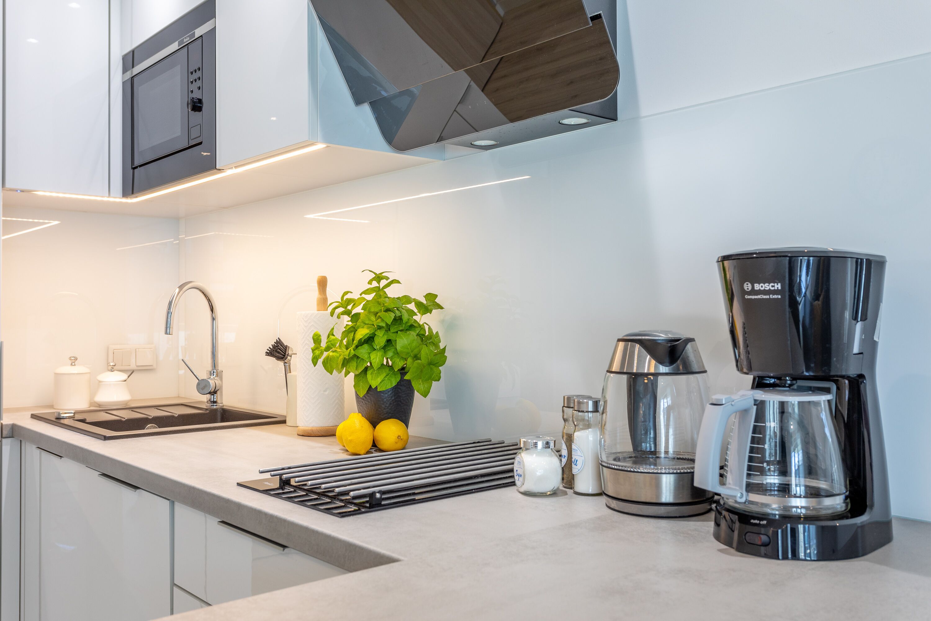 A modern kitchen with a Bosch coffee maker, a sink, a potted plant, and a kettle.