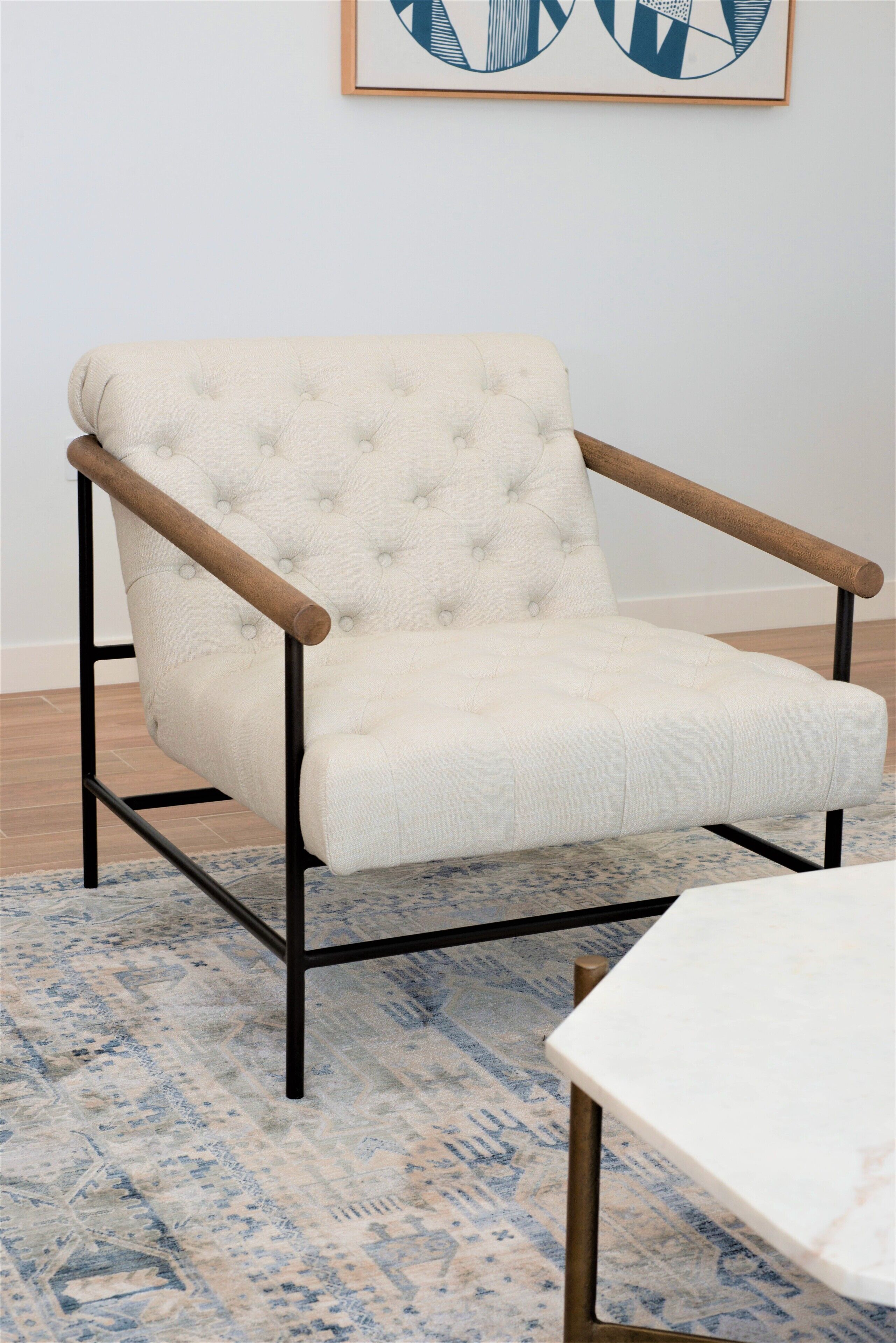 A tufted armchair with wooden armrests and metal frame, placed on a patterned rug.