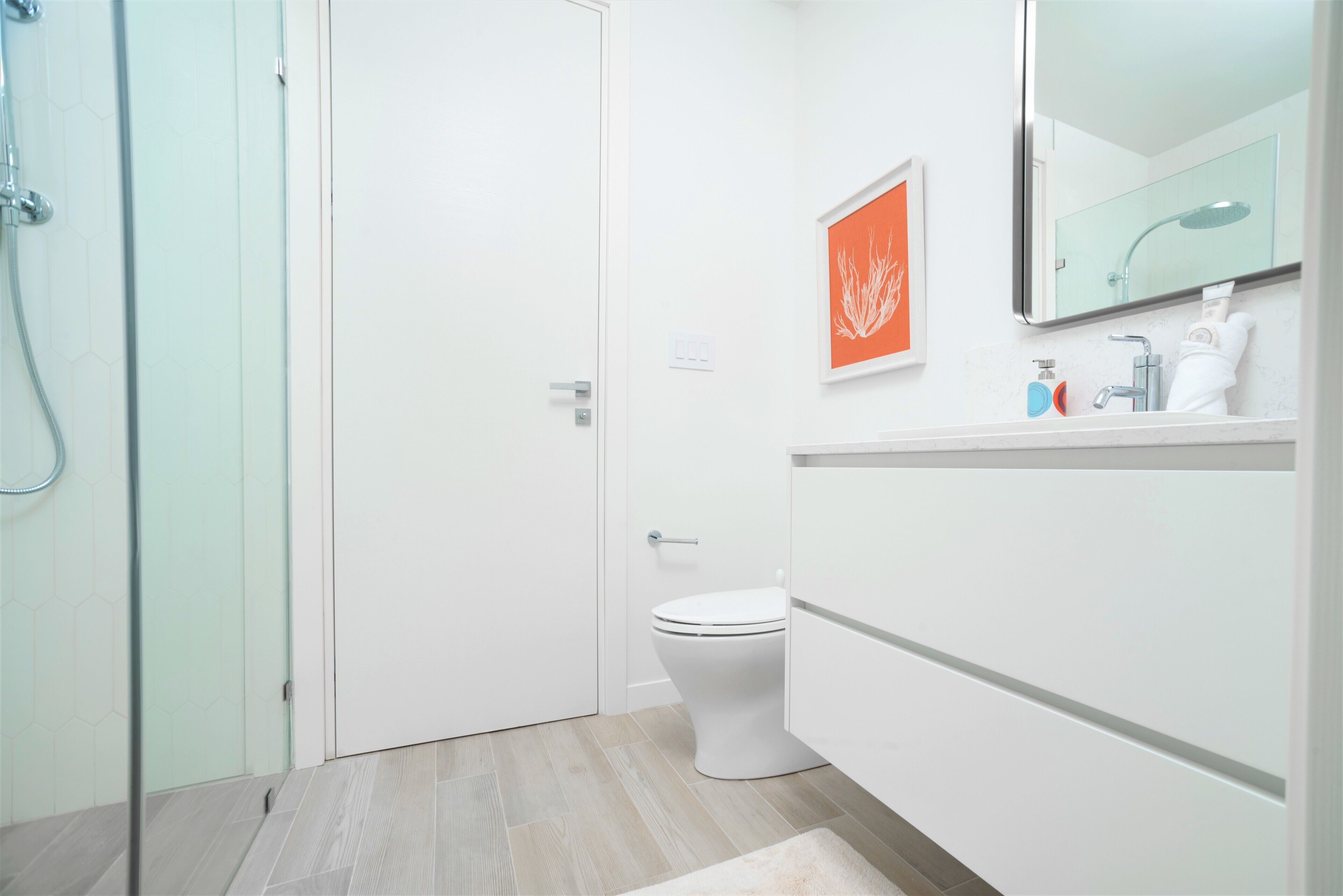 A modern bathroom with a glass shower enclosure, a white toilet, and a vanity with a mirror and towel rack.