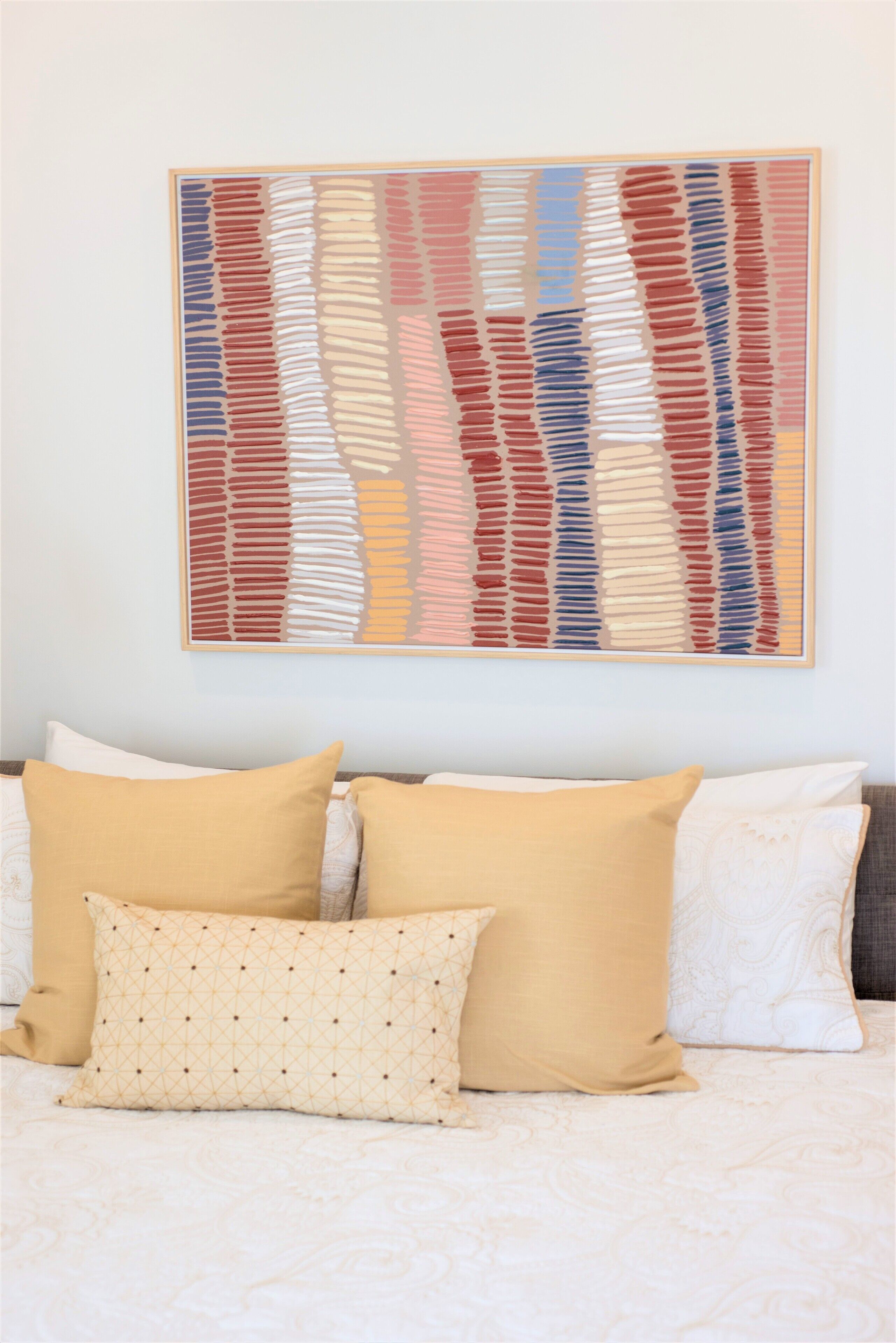 Un dormitorio con cama, dos almohadas y un cuadro abstracto colgado en la pared.