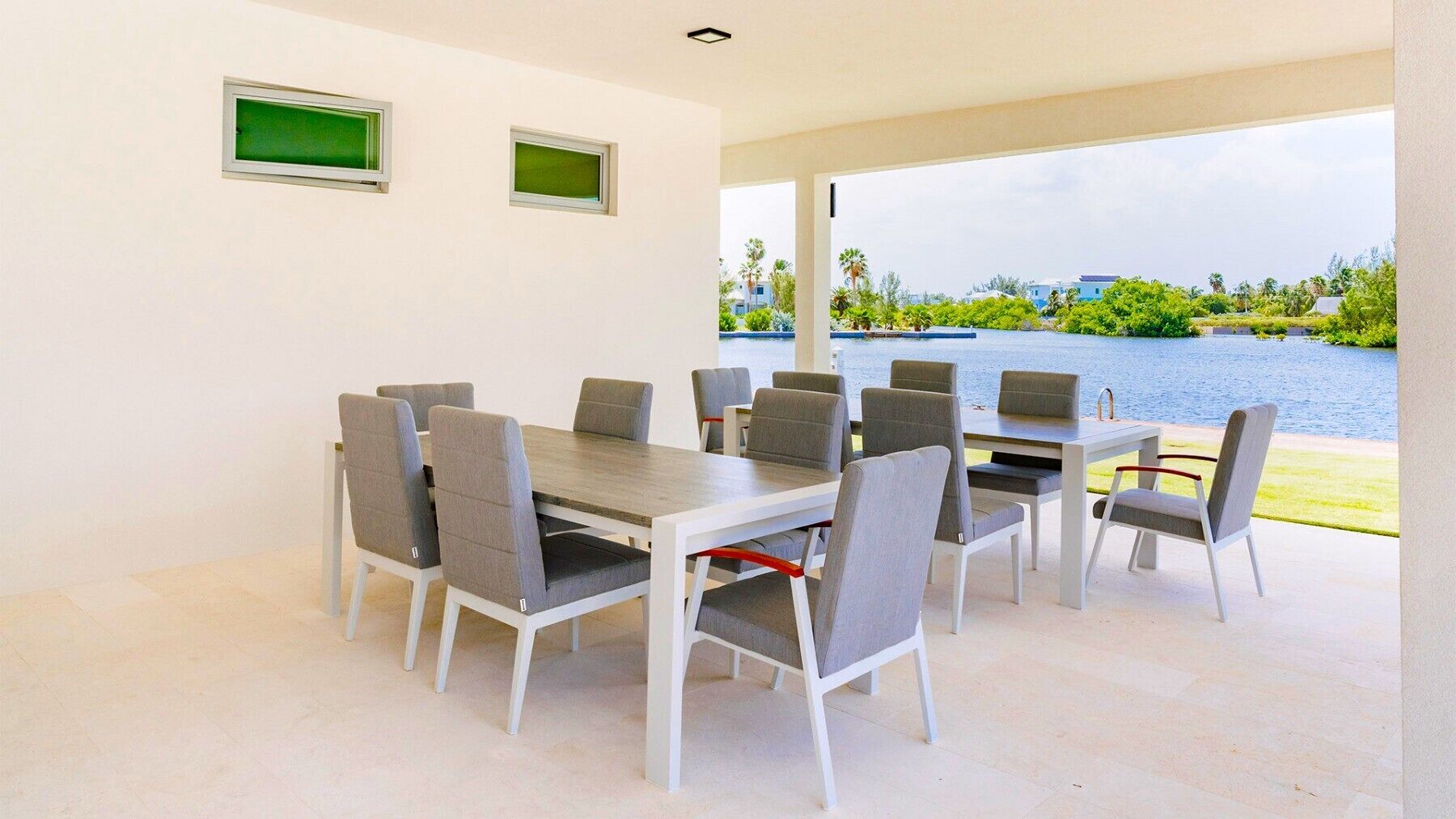 Un comedor con una mesa y sillas, vista a un cuerpo de agua y una pared blanca con dos ventanas pequeñas.