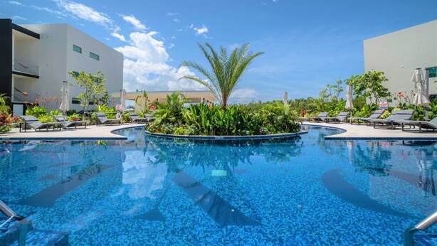 A swimming pool with lounge chairs and umbrellas, surrounded by greenery and modern buildings. - Cayman Luxury Rentals at One Canal Point (Seven Mile Beach)