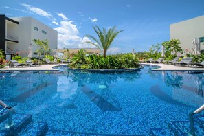 A swimming pool with lounge chairs and umbrellas, surrounded by greenery and modern buildings.