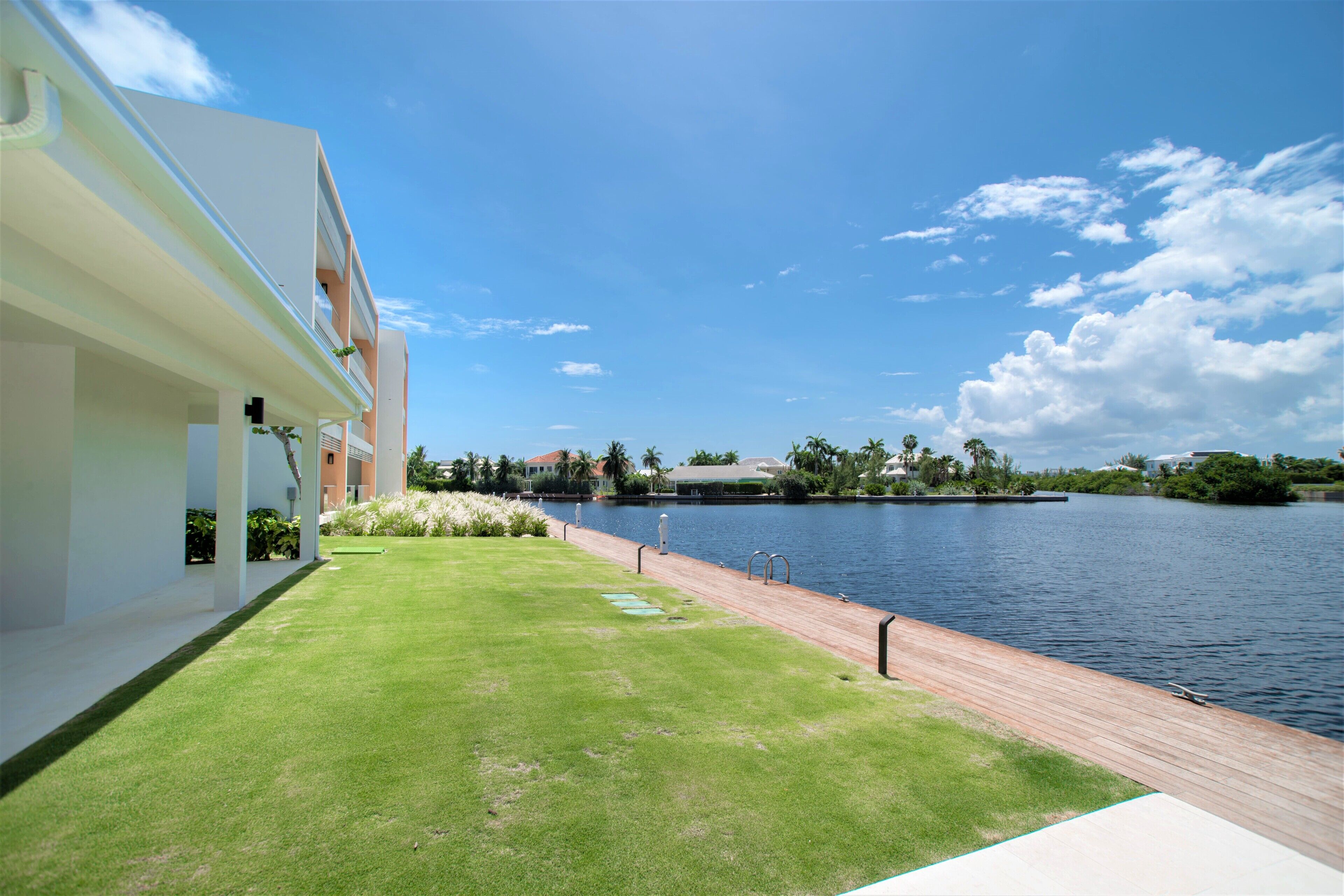 A modern building with a grassy area and a wooden deck overlooking a calm body of water.