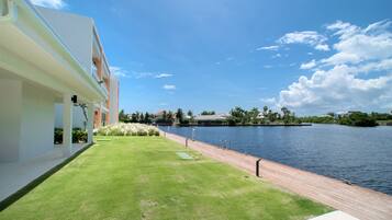 A modern building with a grassy area and a wooden deck overlooking a calm body of water.