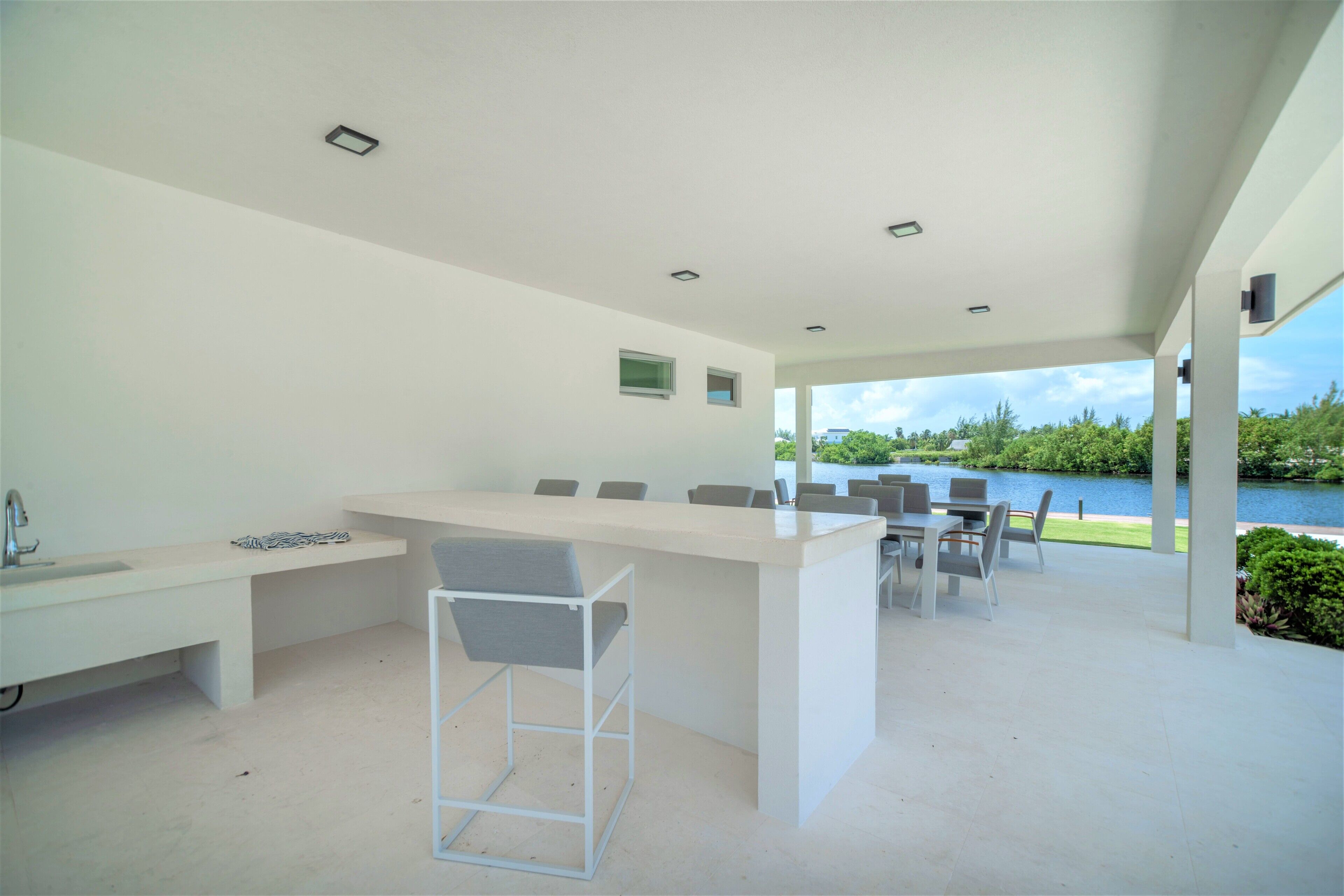 Un espace cuisine extérieur moderne, doté d’un bar, de sièges et offrant une vue sur un lac.